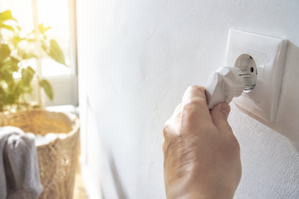 Une main branche une prise électrique blanche dans une prise murale sur un fond clair et lumineux.